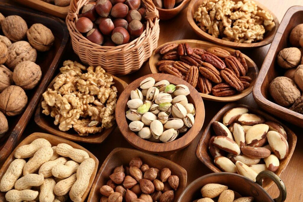 An assortment of nuts are gathered on a table in separate bowls.